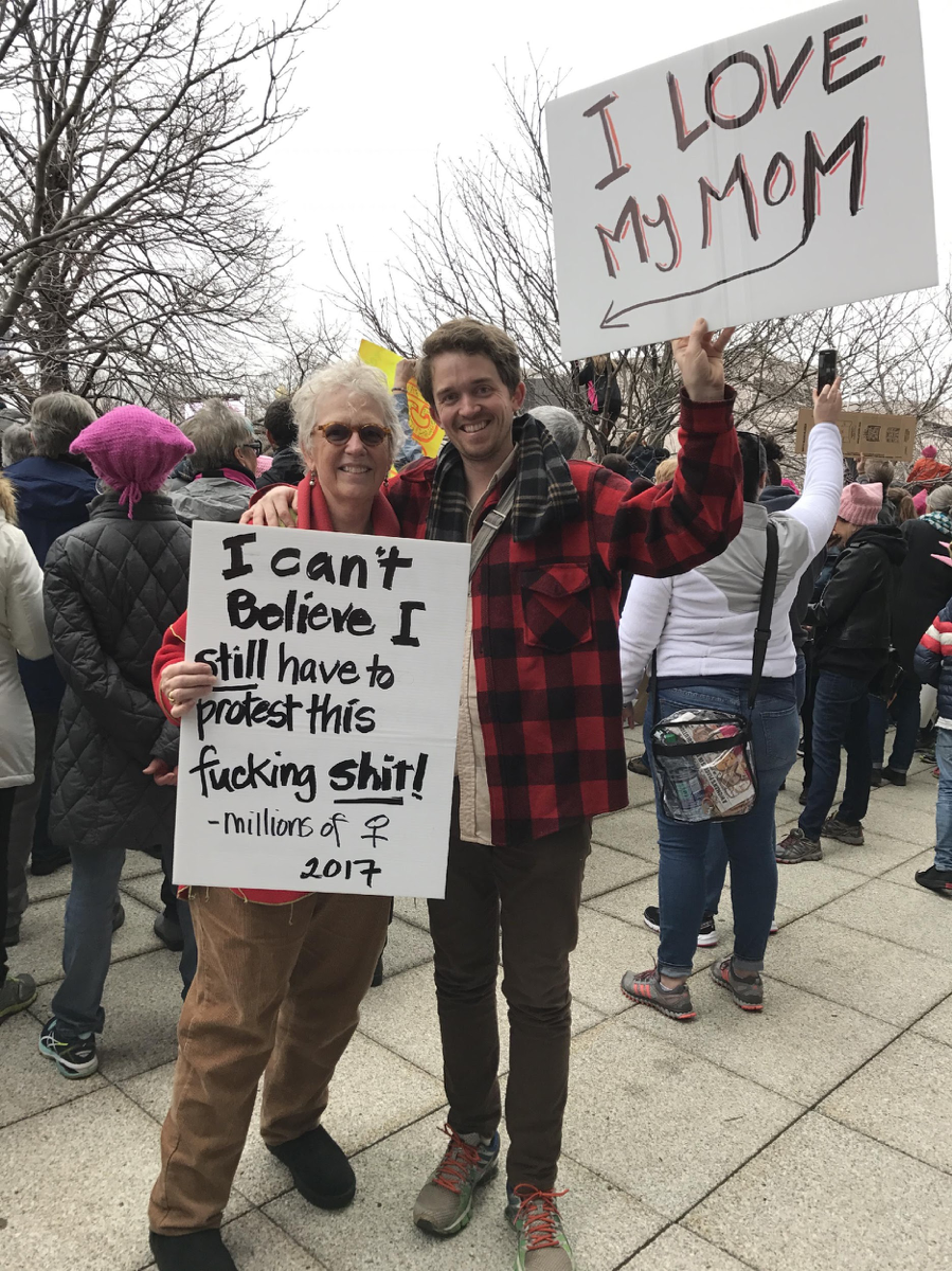 Man and woman with signs: “I can’t believe I still have to protest this fucking shit – millions of women 2017” and “I love my mom” 
